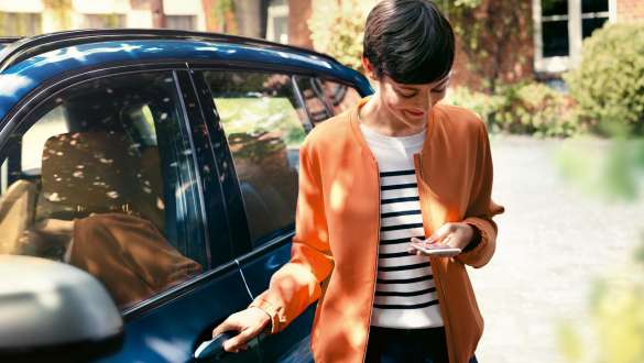 BMW TeleServices BMW TeleServices Mujer con smartphone junto a la puerta de su BMW