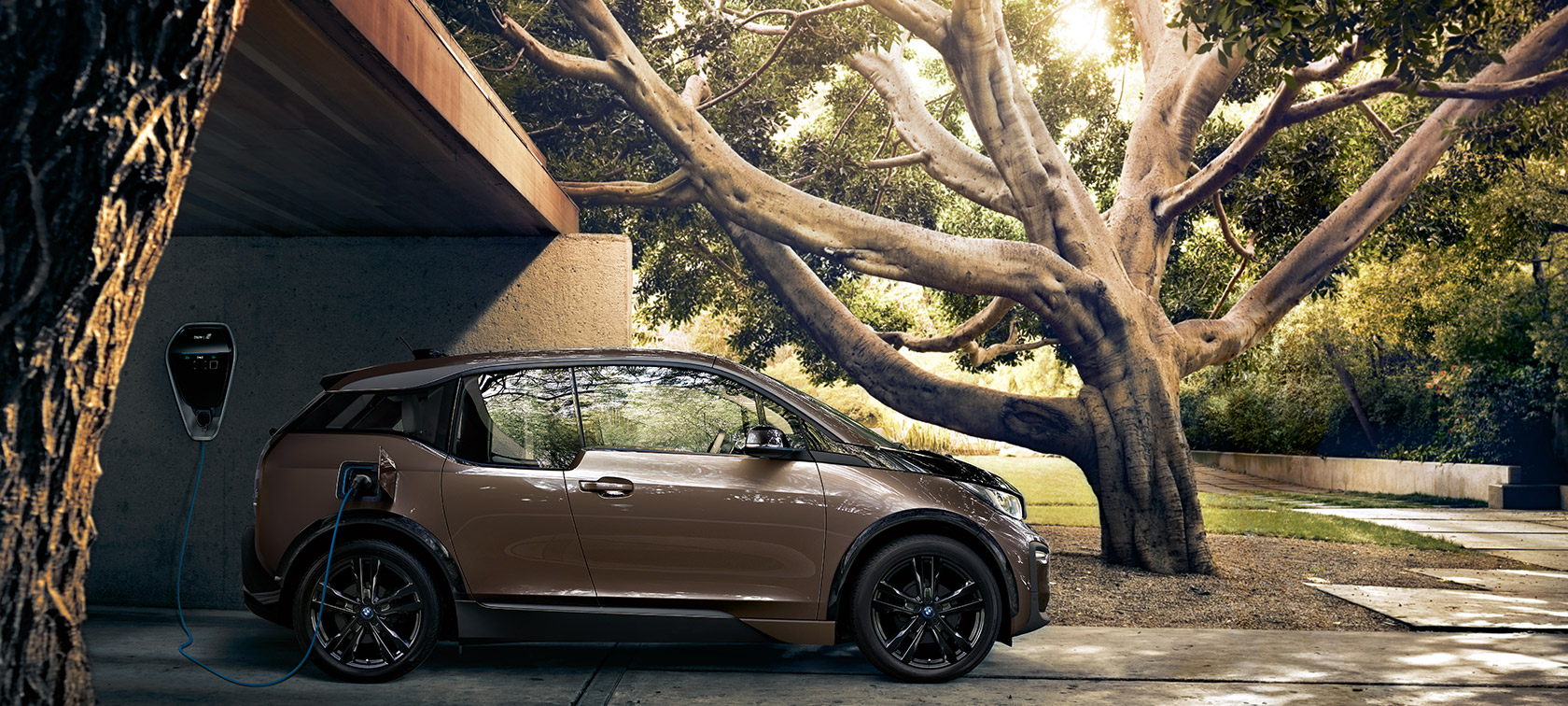 BMW i3s on BMW i Wallbox. BMW i3s in side view on BMW i Wallbox in front of nature setting.